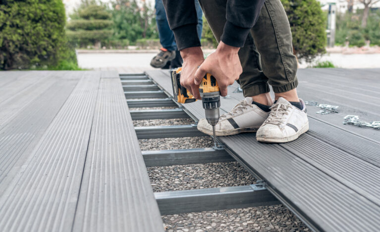 Man assembling composite deck using cordless screwdriver.